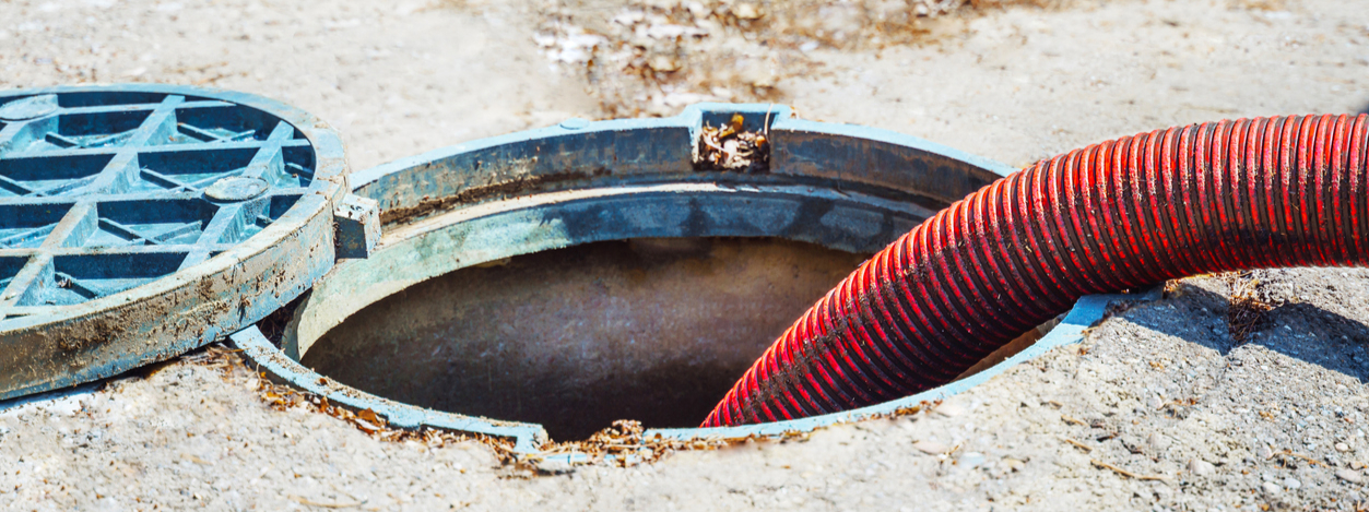 Open manhole with a red hose inserted, on concrete ground. Blue manhole cover is partially open.